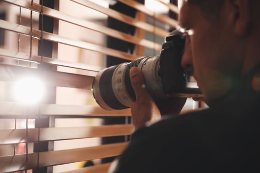 Une personne prend des photos à travers des stores avec un téléobjectif.
