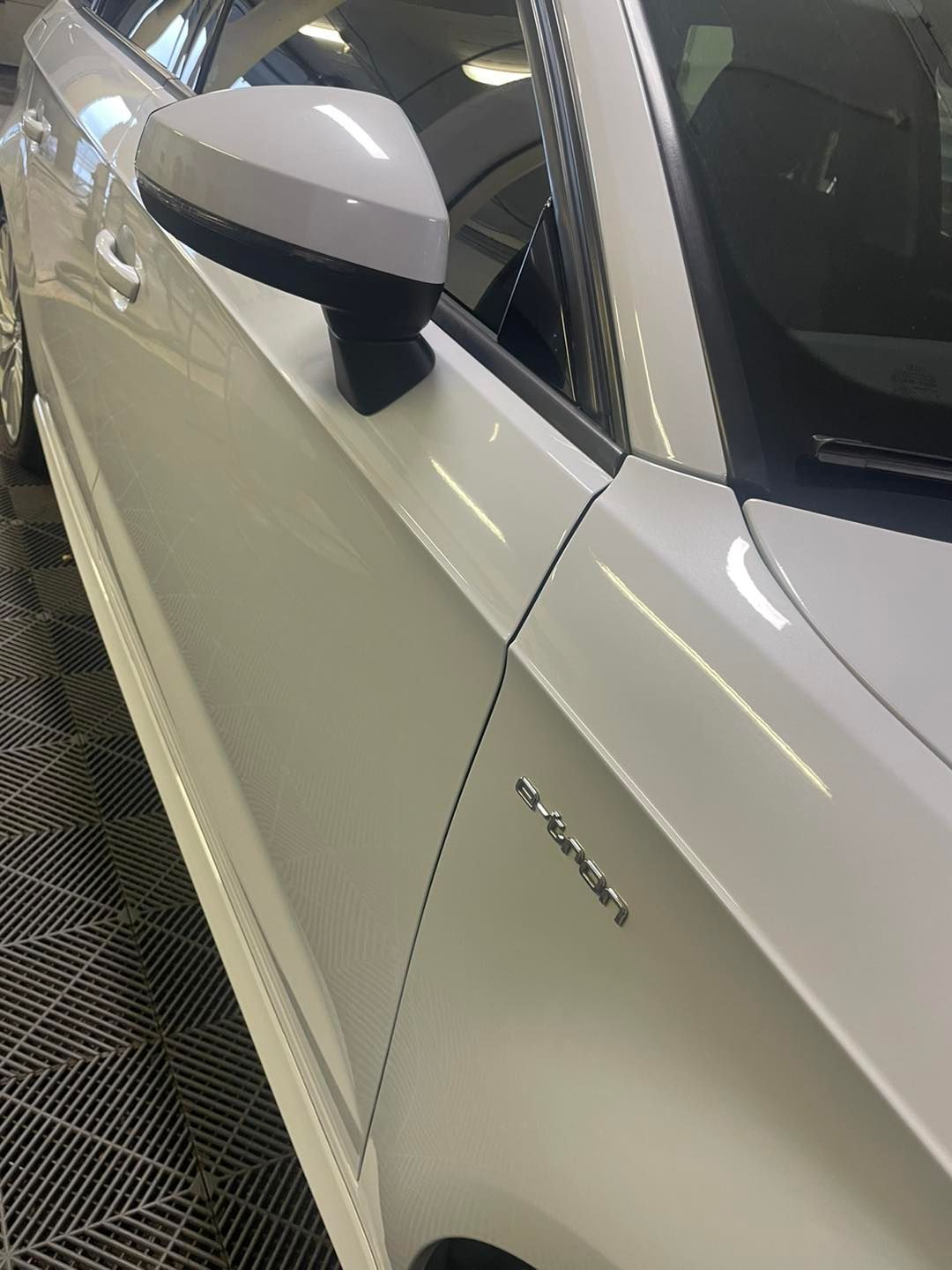 Hvítur bíll stendur á flísum á gólfi í bílskúr.