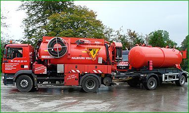 Un camion-citerne rouge vif, avec une remorque rouge assortie, est stationné à l'extérieur, devant un fond d'arbres.