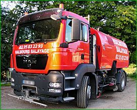 Un camion balayeuse de voirie MAN rouge, portant le nom de la société Halbourg Balayage, est stationné à l'extérieur, devant des arbres.