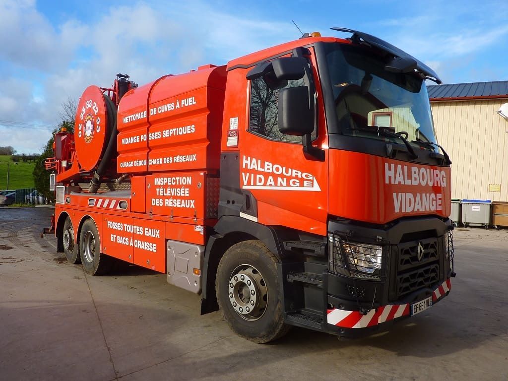 Un camion aspirateur industriel orange vif, portant la marque « Halboug Vidange », est stationné sur un terrain en béton.