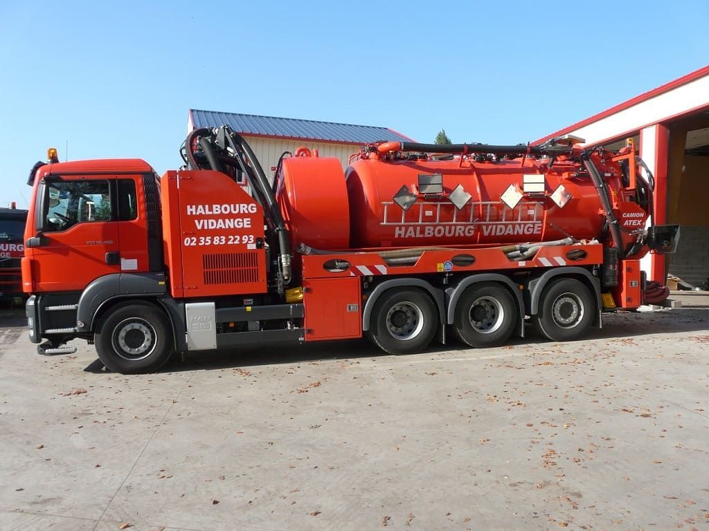Un camion aspirateur orange vif est stationné sur un terrain en béton à côté d'un bâtiment.