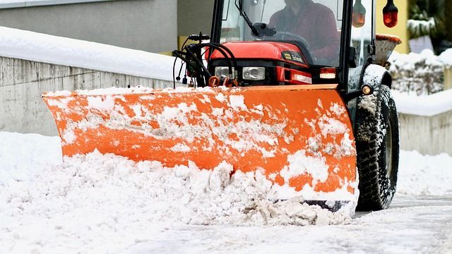 Une déneigeuse orange vif, attelée à un tracteur, dégage un passage dans la neige sur une route asphaltée.