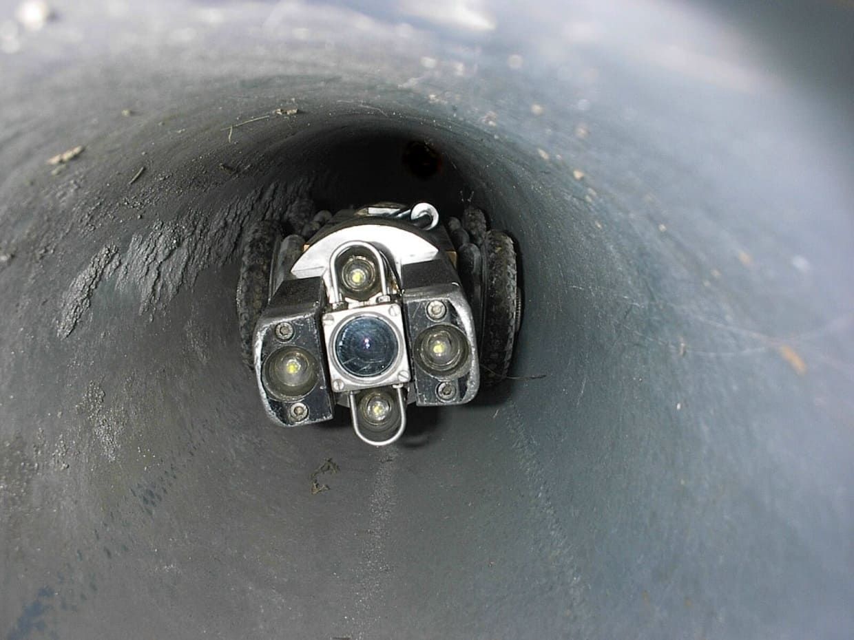 Une caméra d'inspection des égouts équipée de lumières LED intégrées se déplaçant dans un tuyau cylindrique sombre.
