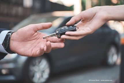 Autoschlüssel übergeben: Zwei Hände tauschen vor einem grauen Auto die Schlüssel aus.