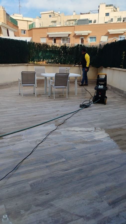 Un hombre está limpiando una terraza de madera con una aspiradora.