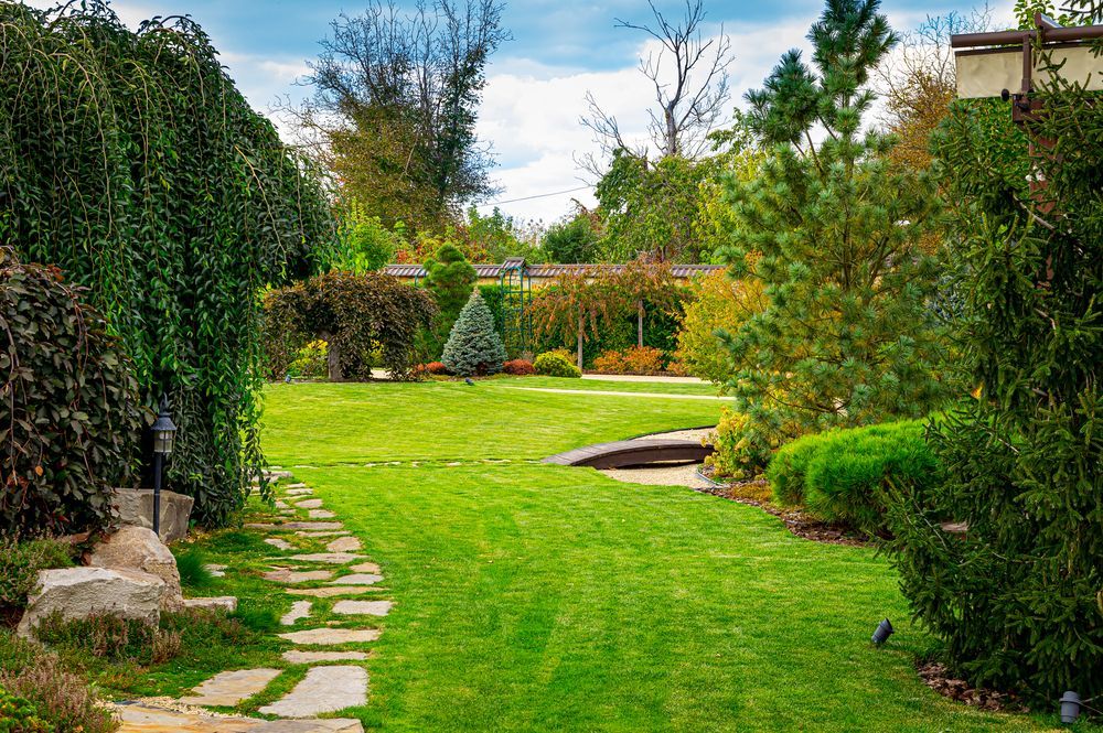 Un camino de piedra que conduce a un gran campo verde exuberante en un jardín.