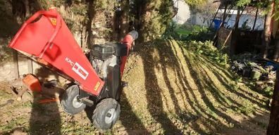 Una trituradora de madera roja está colocada encima de una pila de madera.