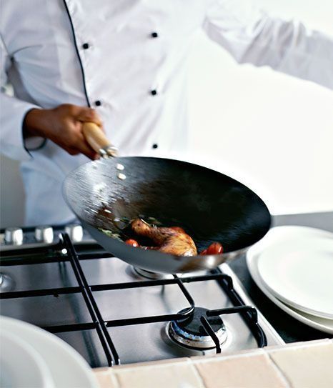 Un chef está revolviendo comida en un wok sobre una estufa.