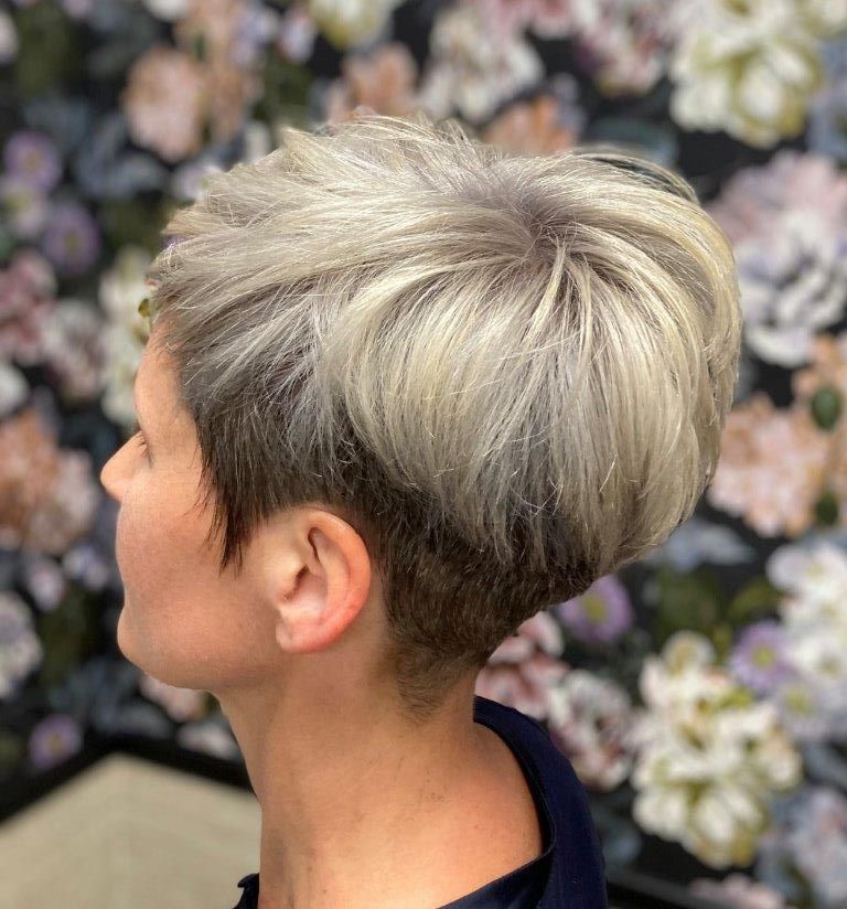 Frau mit kurzem, strukturiertem, hellfarbigem Haar, an den Seiten kurz geschnitten, vor einem floralen Hintergrund.