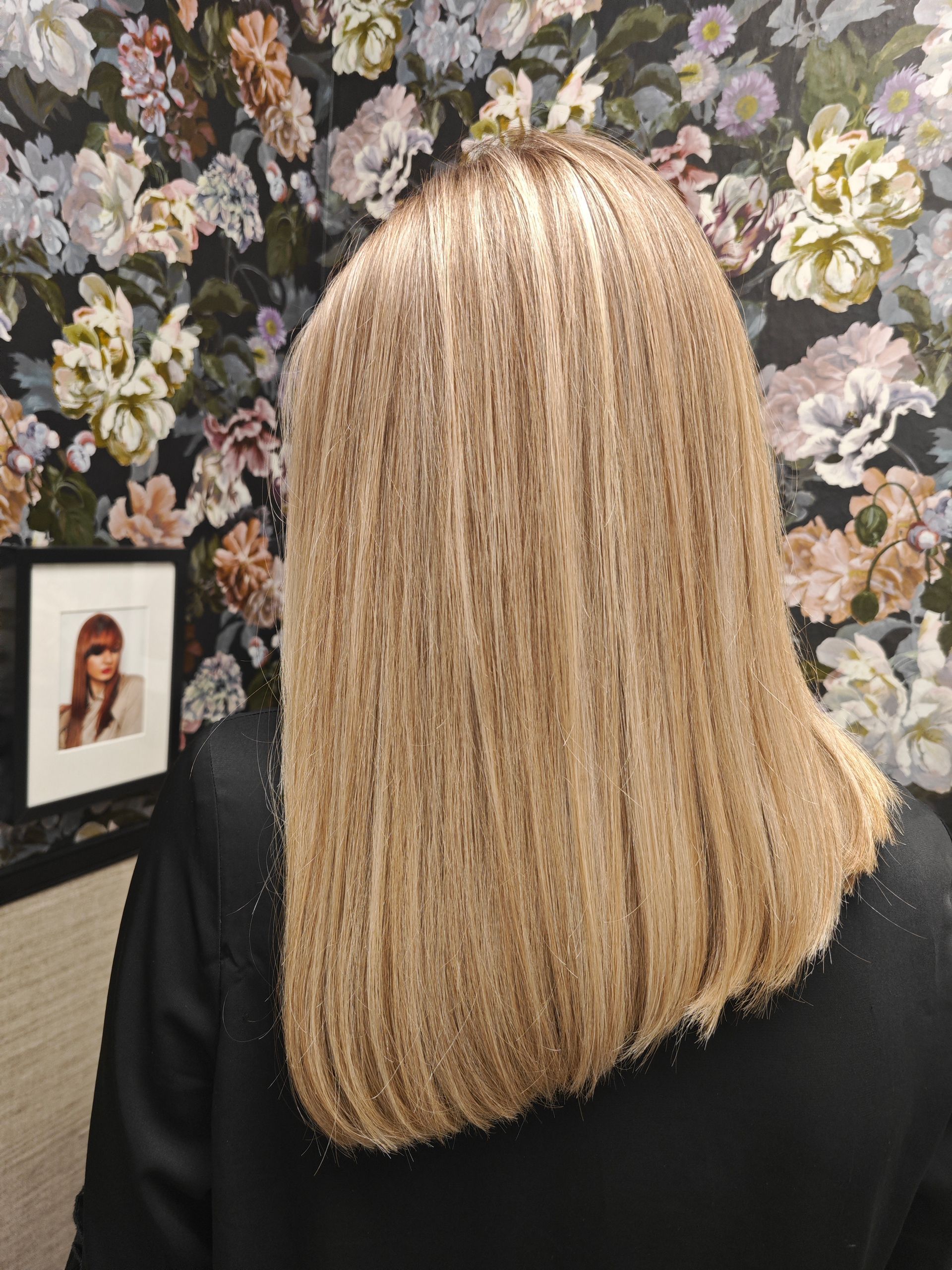 Blondes, glattes, schulterlanges Haar vor einer floralen Tapete.