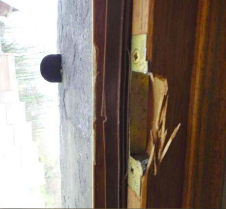 Gros plan sur un cadre de porte en bois endommagé et son loquet, la peinture s'écaillant et le bois étant fendu.