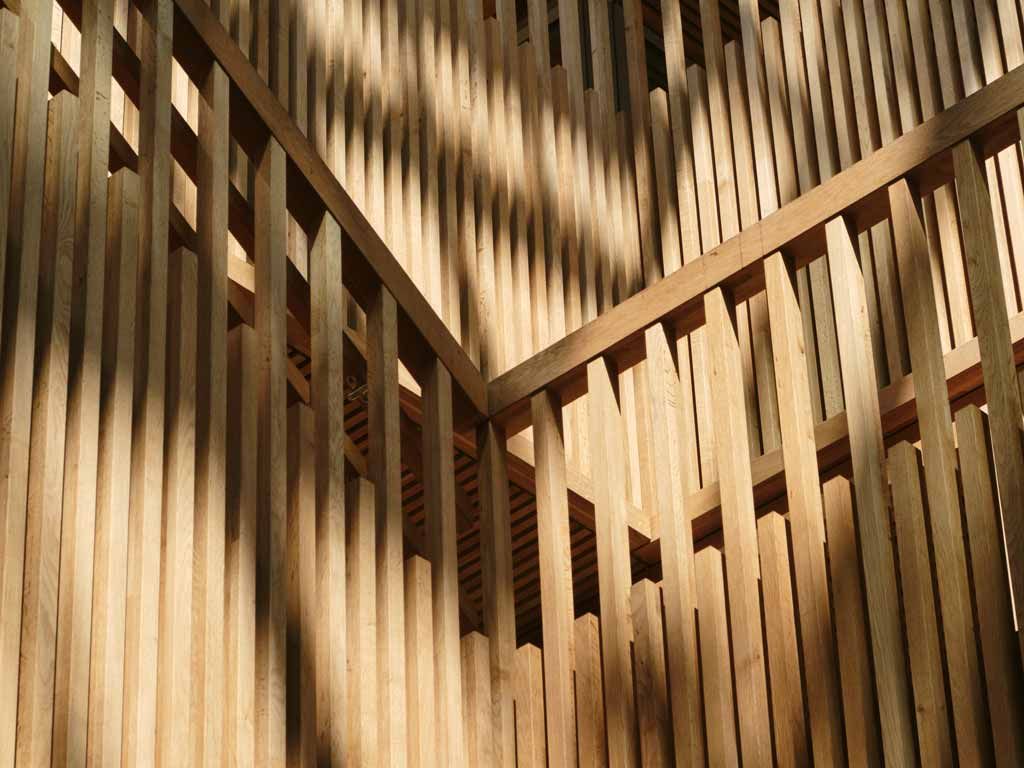 Structure en bois avec poutres verticales et rambarde, projetant de longues ombres au soleil.