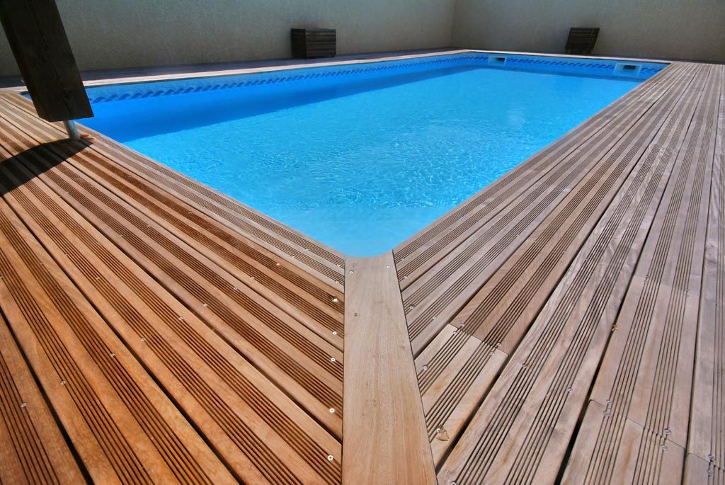 Une terrasse en bois entoure une piscine rectangulaire aux eaux d'un bleu éclatant.