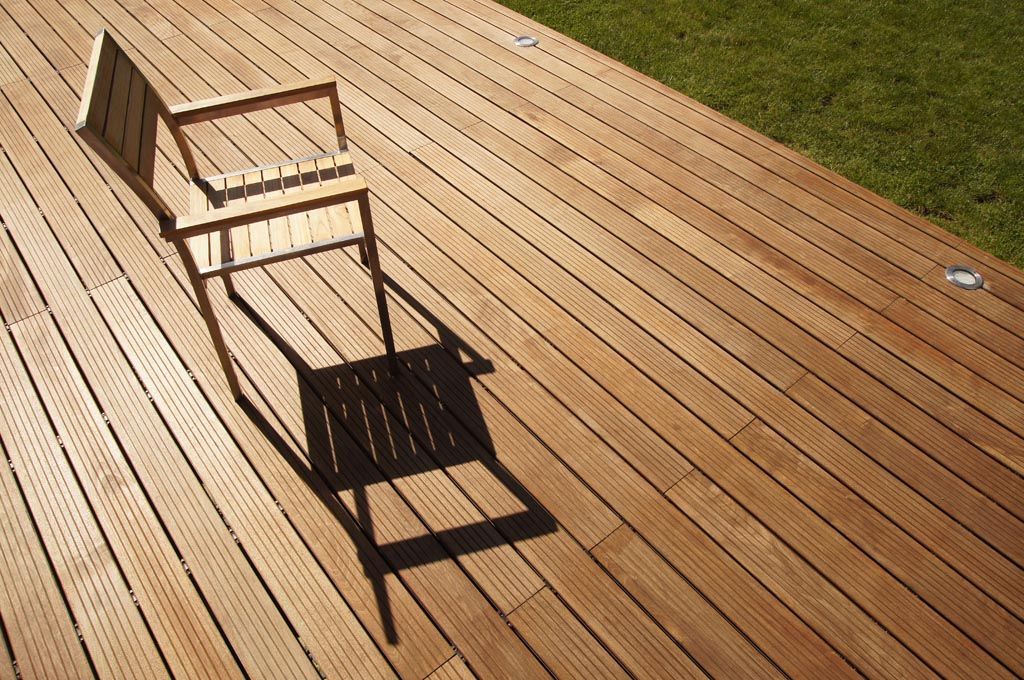 Terrasse en bois avec une chaise projetant une longue ombre par une journée ensoleillée. De l'herbe verte borde la terrasse.
