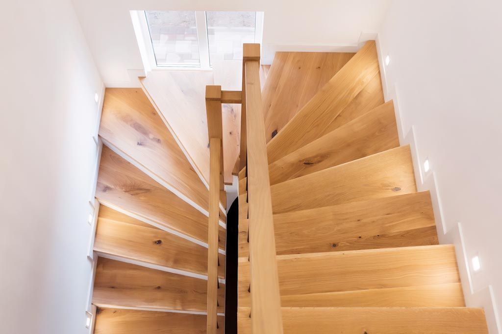 Escalier en bois avec contremarches blanches, rampe en acier inoxydable et plante en pot dans un panier tressé.