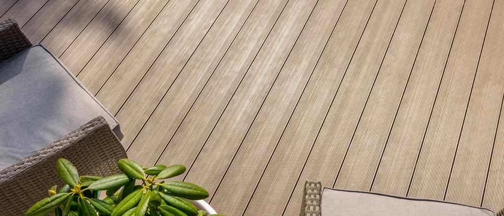 Terrasse en bois à rainures diagonales, partie d'une chaise et plante verte visibles.