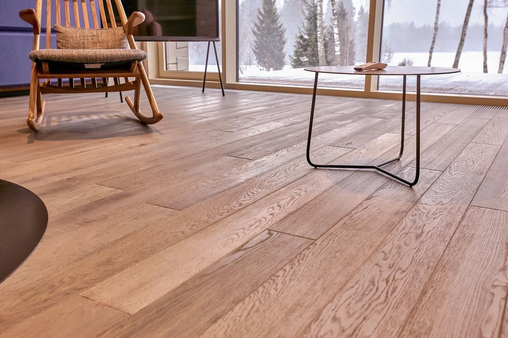 Sol en bois, fauteuil à bascule et petite table dans une pièce offrant une vue sur un paysage enneigé.