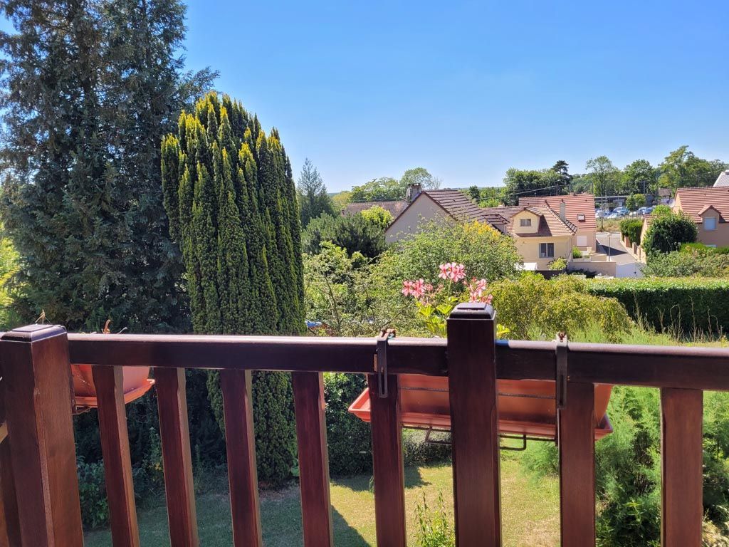 Vue depuis le balcon sur des maisons de banlieue et une végétation luxuriante par une journée ensoleillée.