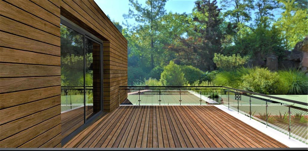 Terrasse en bois avec balustrade en verre donnant sur un paysage verdoyant et un bâtiment moderne en bois.