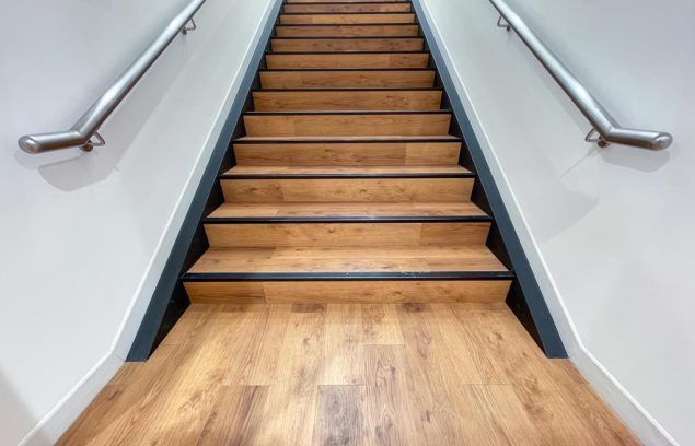 Escalier en bois avec rampes montant entre des murs blancs.