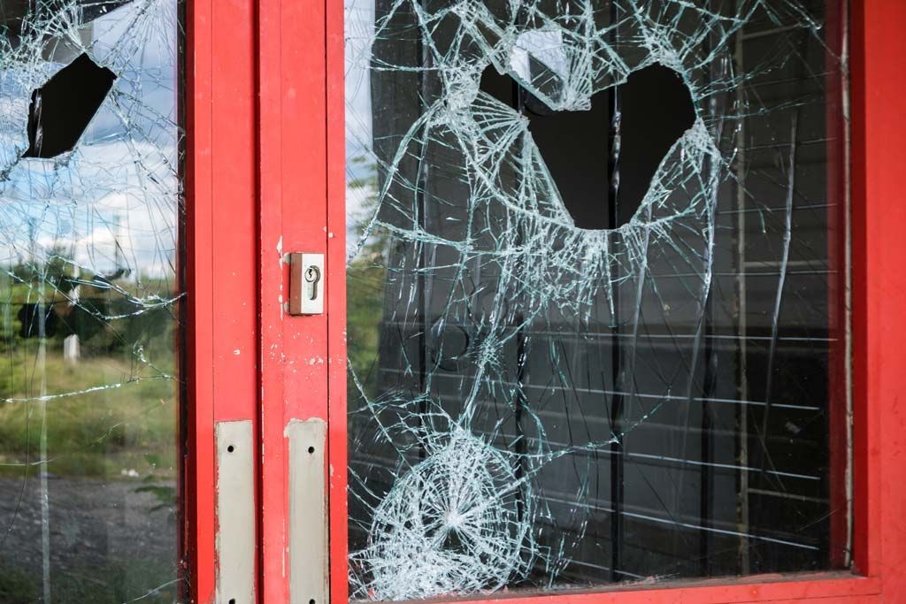 Porte rouge avec vitre brisée ; probablement un acte de vandalisme ou une effraction.