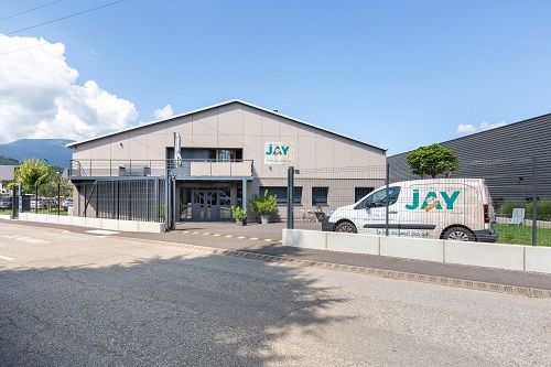 Bâtiment industriel gris avec le logo JAY et une camionnette blanche portant le logo.