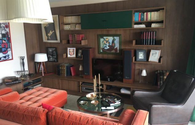 Salon avec canapé orange, meuble mural en bois contenant des livres, une télévision et des œuvres d'art.