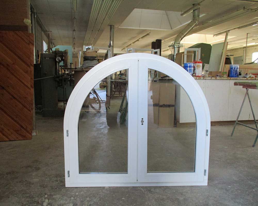 Fenêtre blanche cintrée à double vitrage dans un atelier lambrissé avec des outils.