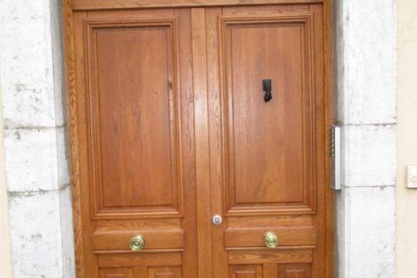 Double porte en bois avec poignées en laiton et heurtoir noir, encadrée de pierre.