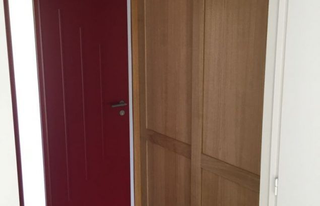 Porte rouge fermée à côté d'une armoire en bois ouverte. Lumière venant de la droite.