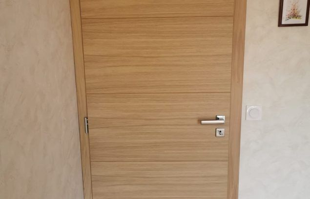 Porte en bois à grain horizontal, poignée argentée et petite décoration murale.