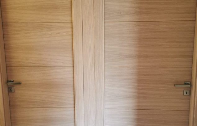 Deux portes en bois clair à panneaux horizontaux et poignées en laiton ; un panneau vertical court entre elles.