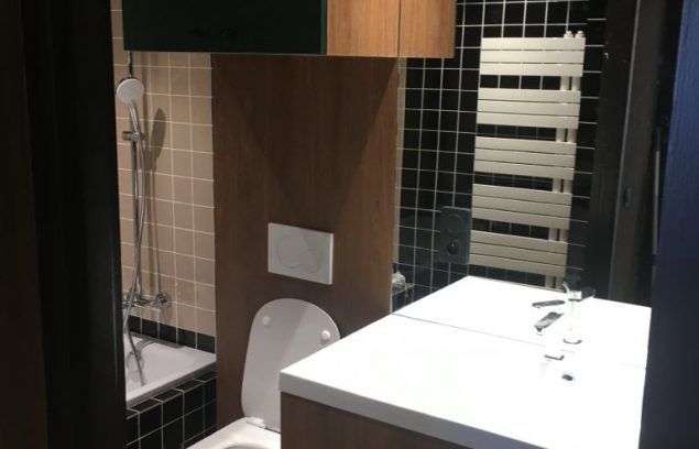 Petite salle de bains avec toilettes, lavabo et baignoire. Les murs sont carrelés et un miroir est placé au-dessus du lavabo.