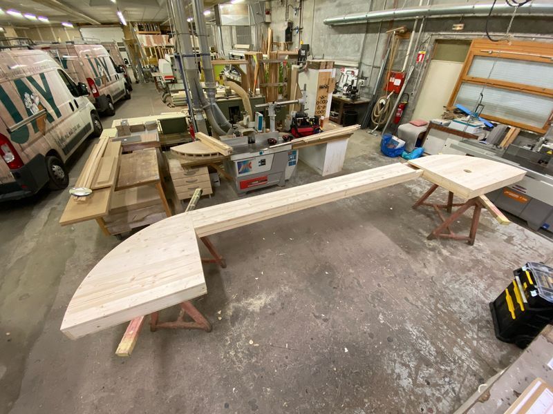 Atelier avec une grande structure en bois sur des tréteaux. Plusieurs autres outils de menuiserie et véhicules sont visibles en arrière-plan.