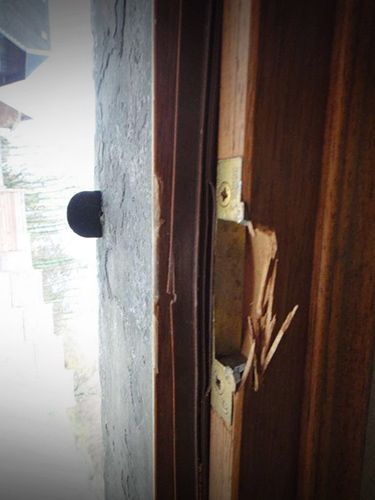 Cadre de porte avec loquet cassé et bois ébréché.