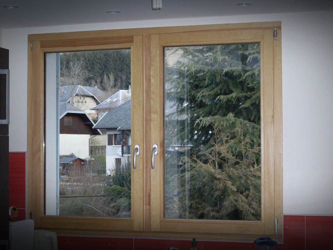 Fenêtre à double vitrage avec cadres en bois donnant sur un village et des arbres.