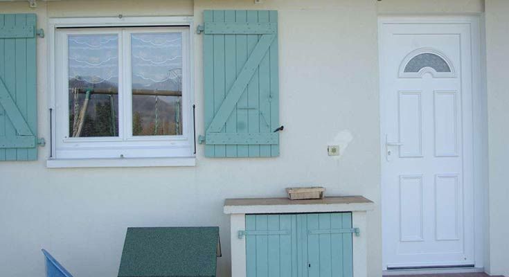 Extérieur d'une maison de couleur claire avec une porte blanche, une fenêtre à volets turquoise et une armoire de rangement turquoise.