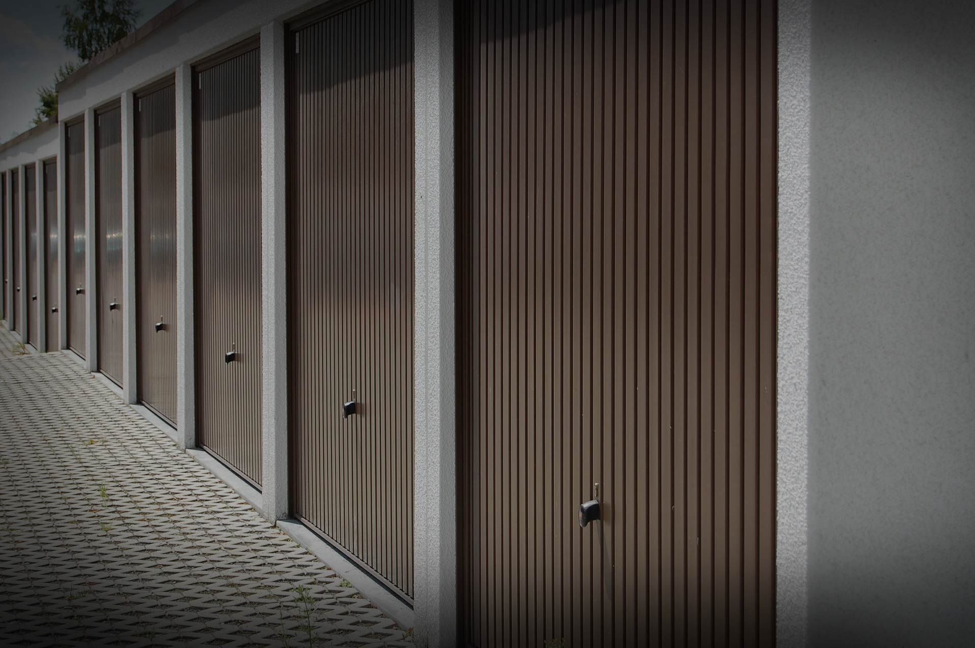 Rangée de portes de garage brunes à rayures verticales, encadrées de béton, vue en biais.