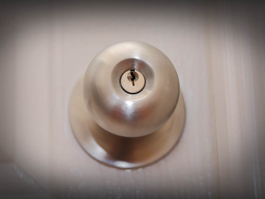 Poignée de porte argentée avec trou de serrure centrée sur une porte couleur crème.