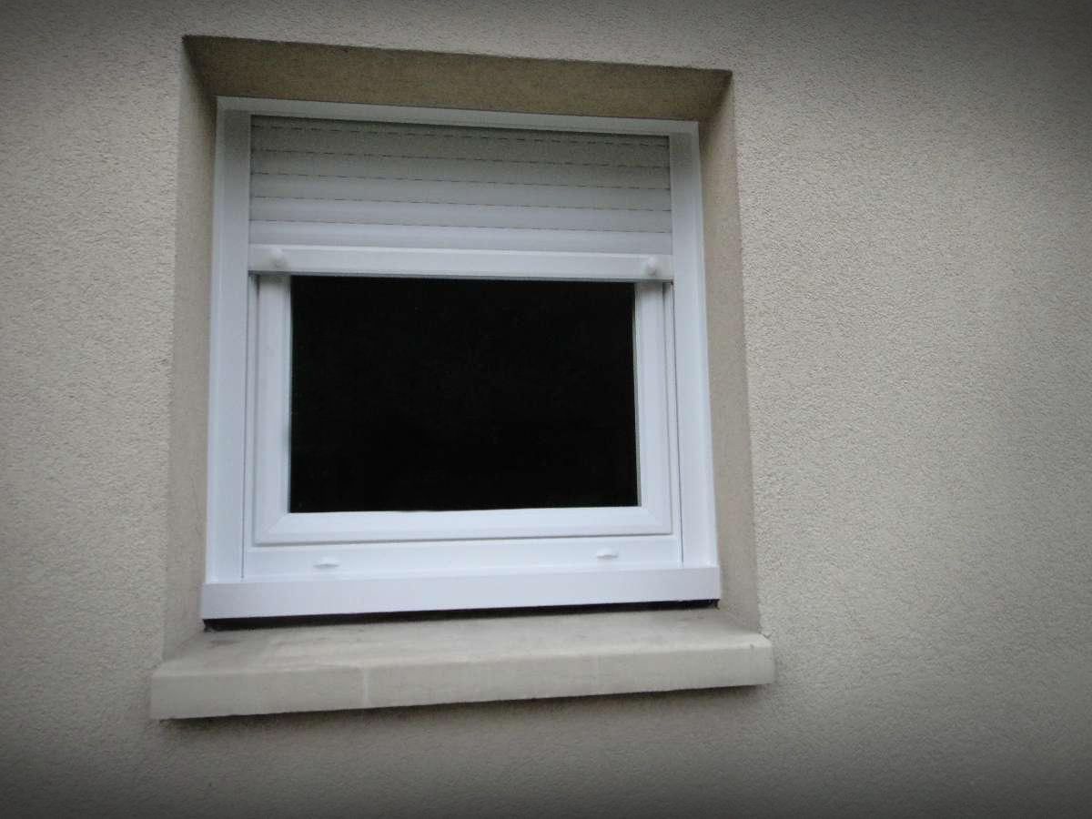 Fenêtre avec stores blancs fermés, encadrée de blanc sur un mur extérieur beige.