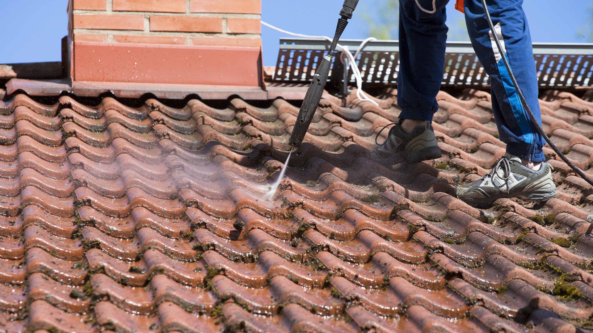 Professionnel sur un toit qui fait nettoie des tuiles sales