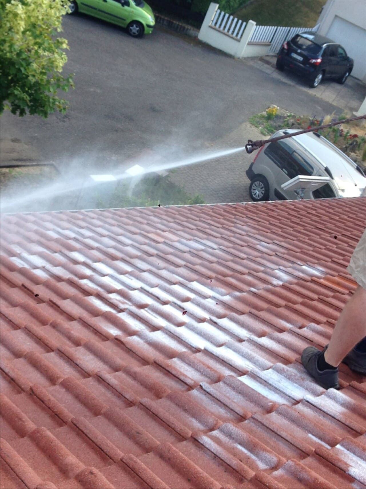 Un couvreur nettoie à haute pression un toit de tuiles rouges