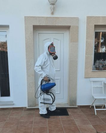 Un hombre que lleva una máscara de gas y un traje protector está rociando una casa.