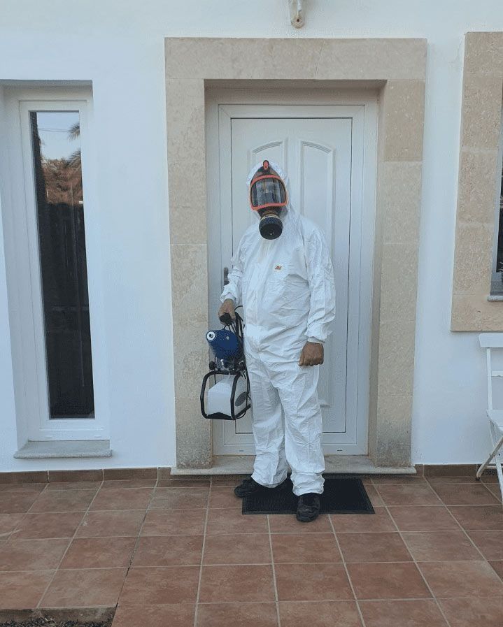 Un hombre con un traje de protección está parado frente a una puerta sosteniendo un rociador.