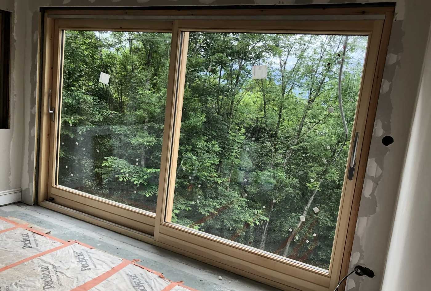 Baie vitrée en double vitrage, structure en bois, vue sur un jardin arboré