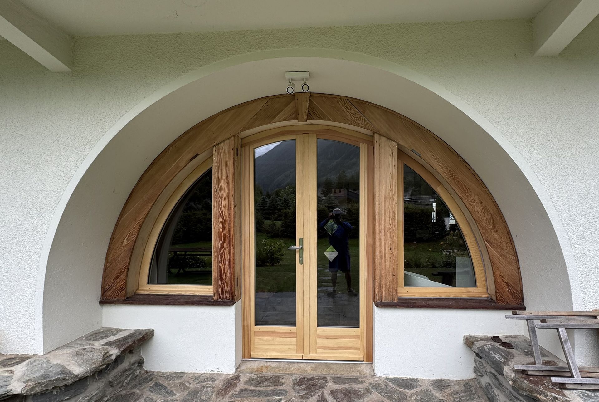Double porte cintrée en bois intégrée à un hall d'entrée en stuc blanc avec sol en pierre et fenêtres des deux côtés