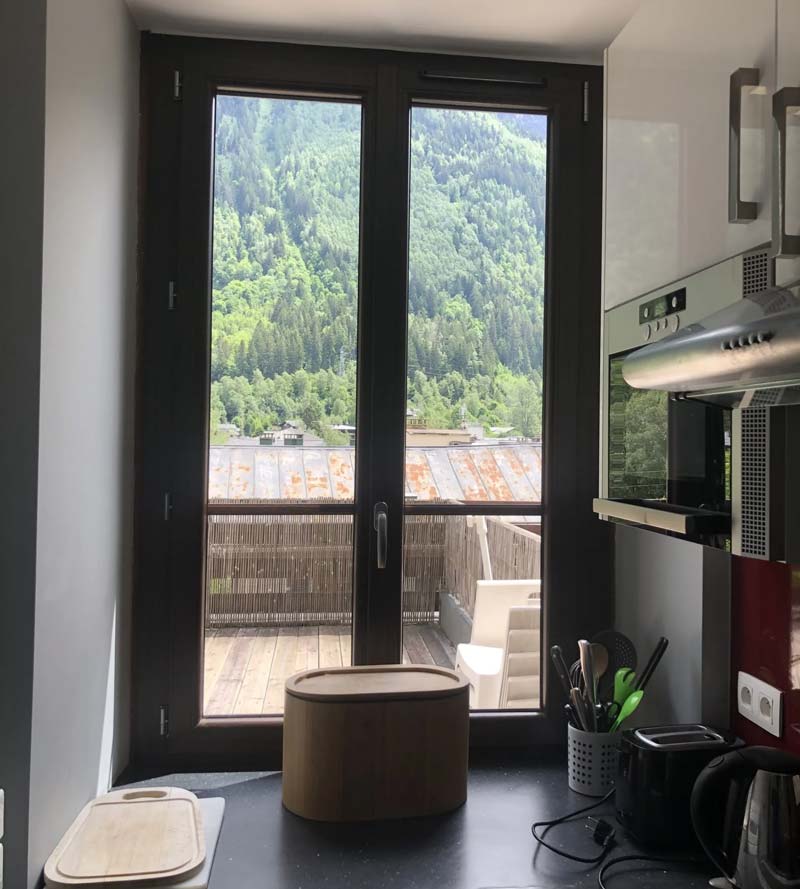 Fenêtre battante noire en PVC, double vitrage, vue sur terrasse et forêt