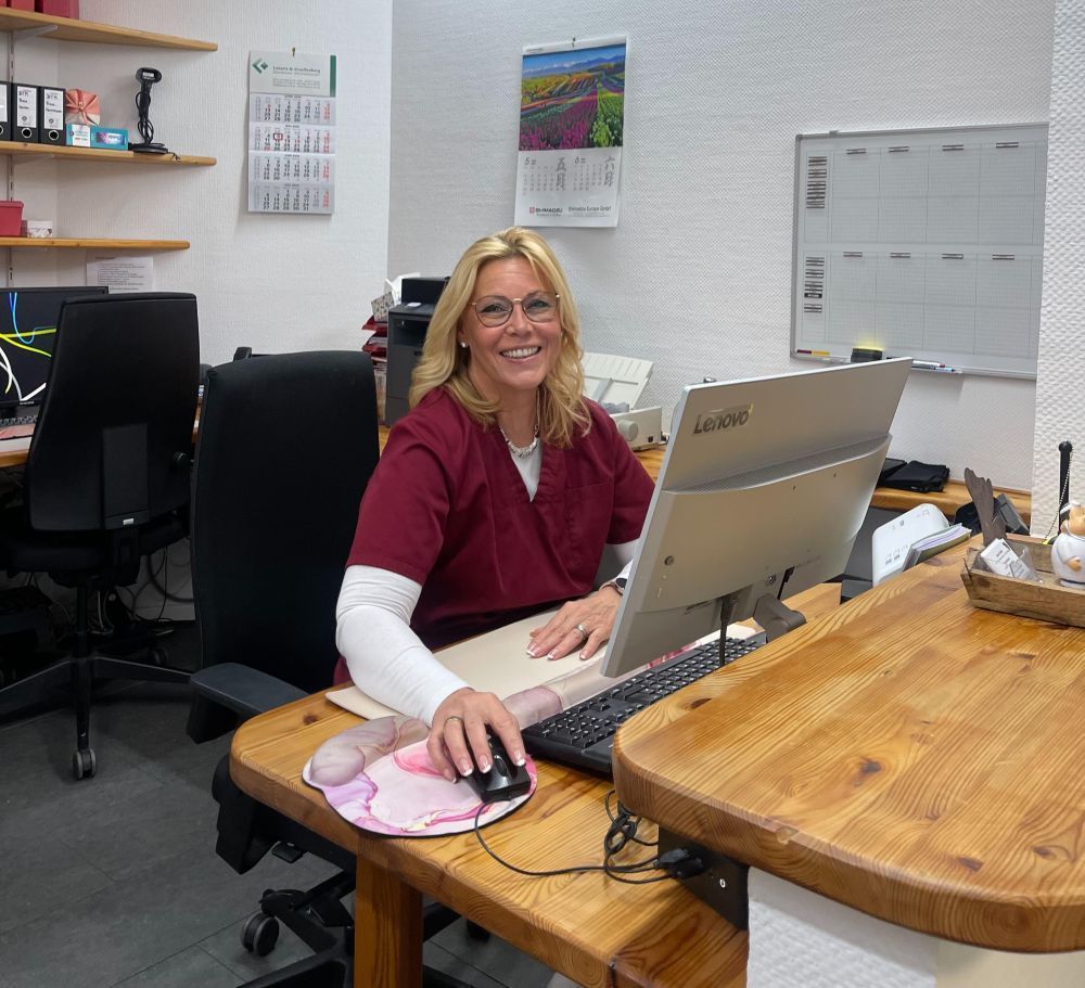 Frau lächelt an ihrem Schreibtisch mit Computer in einem hellen Arbeitsbereich