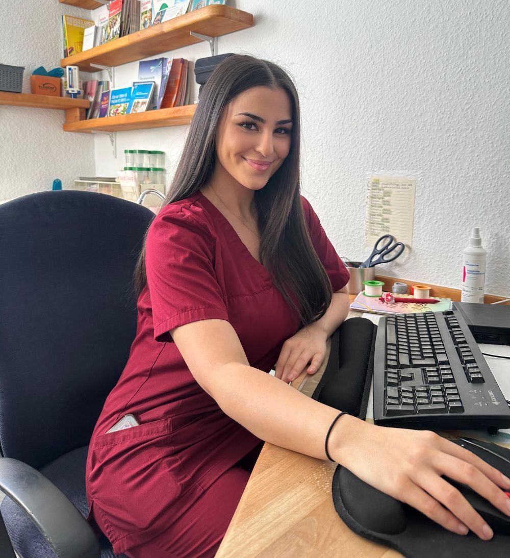 Frau lächelt an einem Schreibtisch, während sie in einem Büro mit Tastatur und Maus arbeitet.